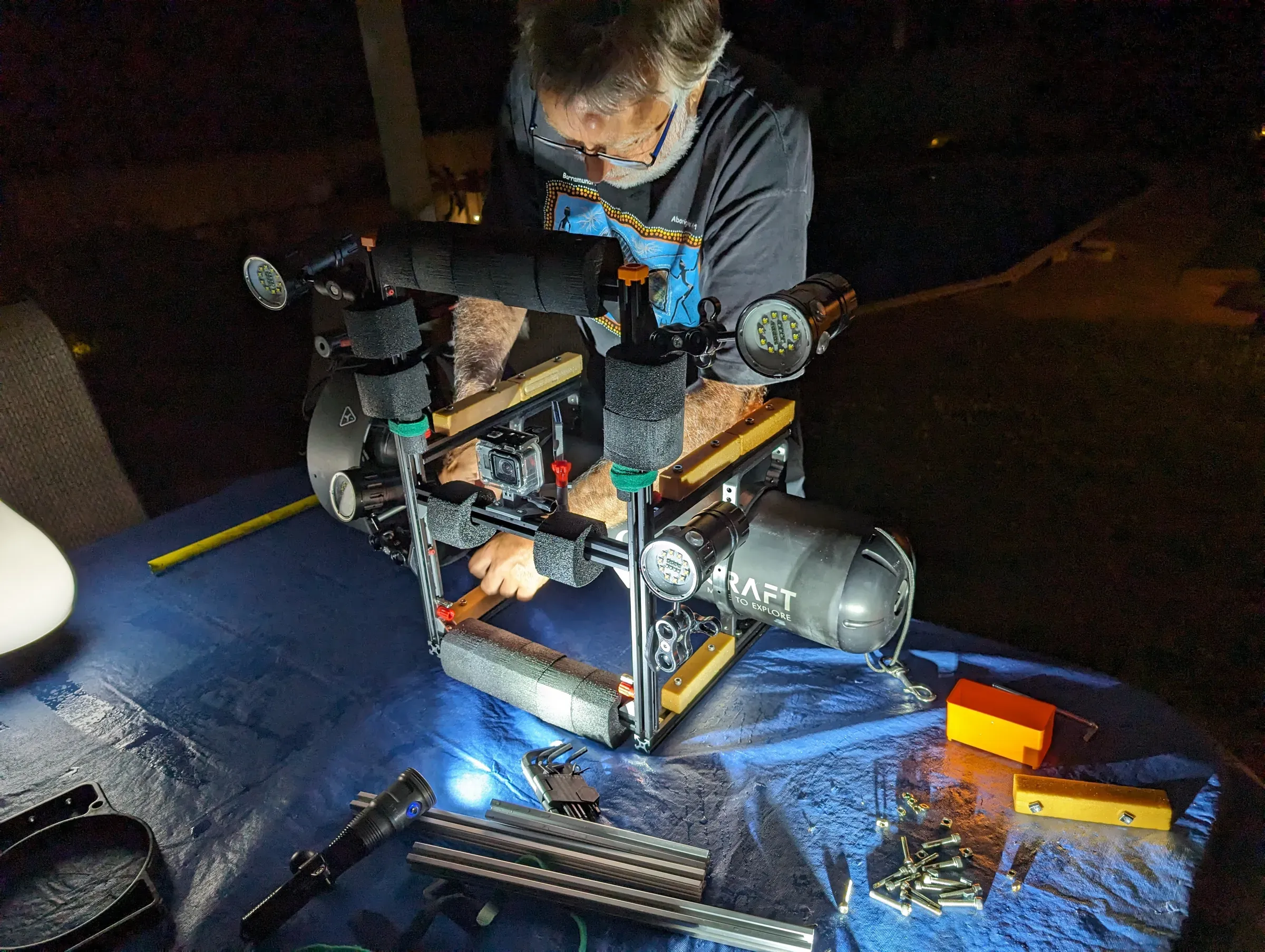 Sylvain Marcotte assemble le rig sur le scooter, de nuit, sur une bâche bleue, les outils autour